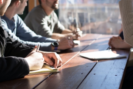 People around a table write on notepads